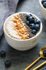 Banana dessert with chia seeds, fresh blueberry and nuts over grey table.