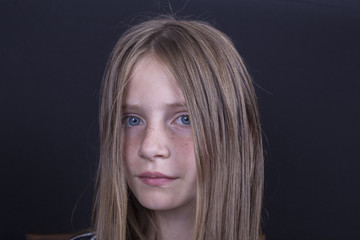 Naklejka premium Beautiful blond young girl with freckles indoors on black background, closeup portrait