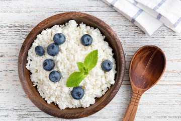 Cottage cheese, ricotta or tvorog with blueberries in wooden bowl on old white wooden table. Top view
