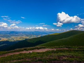 Obraz premium White clouds in the blue sky floating above the mountain peaks stretching to the horizon line