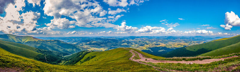 Fototapeta na wymiar Panoramic view of green hills with mountains, large valleys and blue sky with white clouds on it