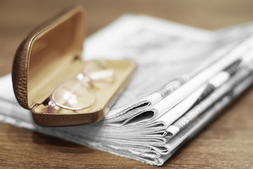 Pile of newspapers and reading glasses in open case, side view, selective focus                    ...