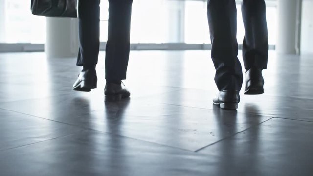 Rear view tilt up shot of two entrepreneurs in formalwear walking with briefcases through the lobby of office center