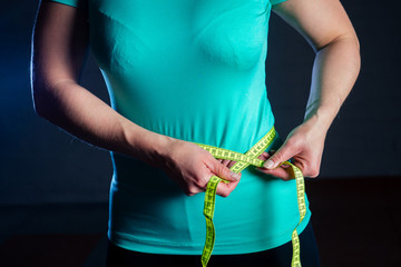 young woman in turquoise t-shirt measures waist with measuring tape