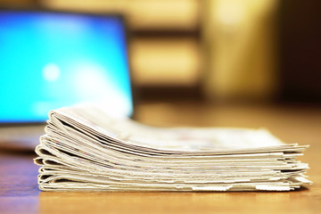 Folded newspapers stacked in pile next to laptop. Computer and daily tabloid journals with news,...