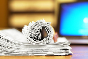 Folded and rolled newspapers stacked in pile next to laptop. Computer and daily tabloid journals...