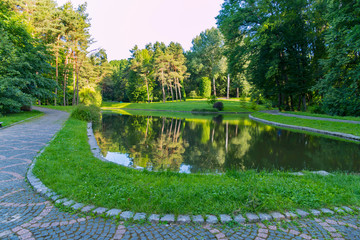 Obraz premium A clean decorative lake in the middle of a walk alley against the backdrop of the forested park trees