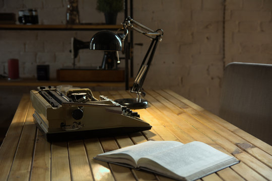 An old typewriter illuminated by a lamp on a wooden lacquered table