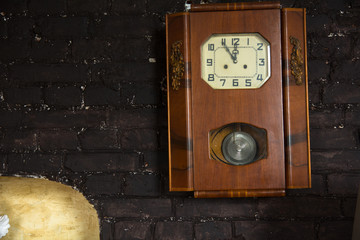 Old wall clock with a pendulum on a brown brick wall background