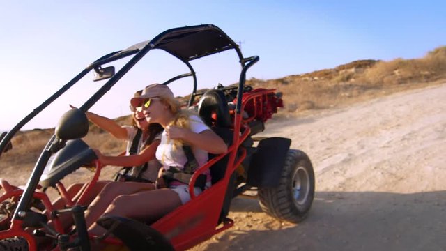Two girlfriends extremely spend holidays driving quadricycle in slow motion. Active women driving buggy car. Young women controlling beach buggy. Courageous women. Extreme ride