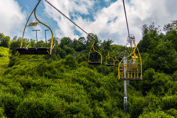 Cable car with cabins for three seats and yellow railings against the backdrop of lush green trees