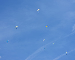 colorful paragliders in expanse of blue sky and white cloud
