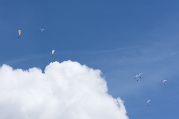 colorful paragliders in expanse of blue sky and white cloud
