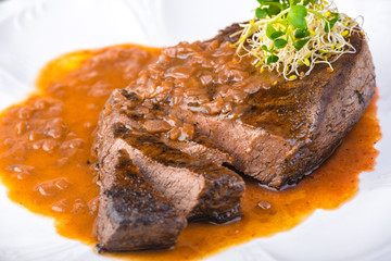 Well-done grilled marinated beef flank steak with sauce on plate