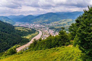 A picturesque view of a rural village and a fast river against the background of high green mountains
