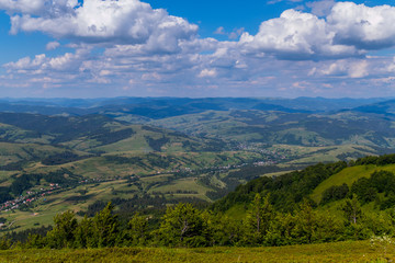 panorama with green mountain ranges and small houses in a valley under a cloudy sky