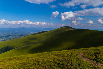 A deep blue sky with white clouds lying over mountain slopes with smooth grass