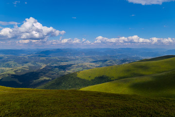 covered with low shrubs mountain slope against the background of distant peaks under clouds in the blue sky. Carpathians