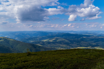 A blue, slightly cloudy sky and beautiful, green mountains with a little haze over them