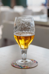 light cold beer in a high glass is on the table on a light background
