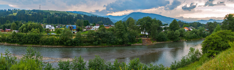 Obraz premium a magnificent panorama of the village lying on the river bank and dense clouds in the sky floating above it