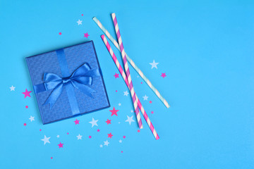 Blue shiny classic gift box with satin bow and cocktail straws with confetti in the shape of stars as attributes of party