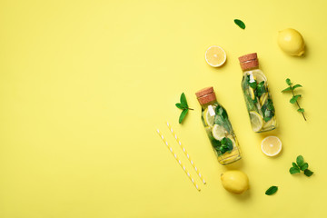 Bottle of detox water with mint, lemon on yellow background. Flat lay. Citrus lemonade. Summer fruit infused water. Top view with copy space.