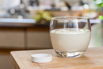 Hand pouring fresh kefir probiotik drink from white bottle into clear glass on kitchen table