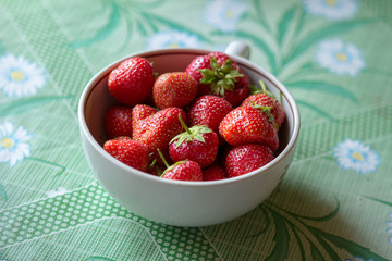 ripe strawberry berry with green leafs in a plate on a green background