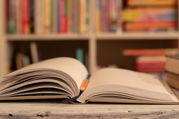 Notepad / book is on a wooden table. orange simple pencil. background, bookcase with colored books