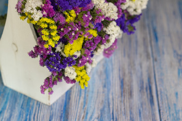 defocus. white wooden basket with colored wildflowers. wooden white \ blue background