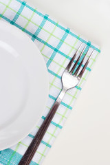 Empty white plate on napkin with fork on white table. Table setting, preparation for food.