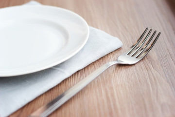 Empty white plate on a gray napkin with fork and glass on brown table. Table setting, preparation for meals.