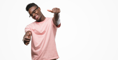 Young african american man wearing pink t-shirt approving doing positive gesture with hand, thumbs up smiling and happy for success. Looking at the camera, winner gesture.