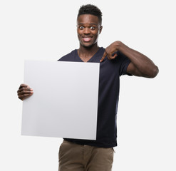 Young african american man holding a banner with surprise face pointing finger to himself