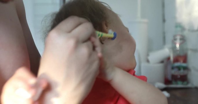 Kid does not want to brush his teeth in crying. Parent brushes his baby boy teeth in the bathroom Close up portrait.