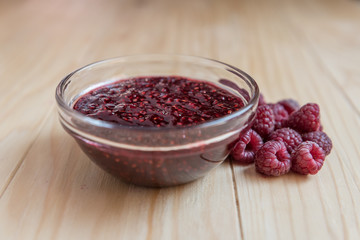 Homemade Raspberry jam in a glass bowl with fresh ripe organic Raspberries  on a wooden table