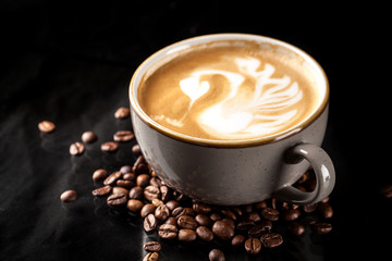 A large cup of expensive ceramics with cappuccino, on top of an art drawing swan from milk. glass on a black mirror background. background image. Copy space