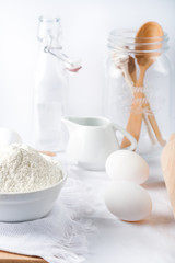  Baking ingredients. White background. Ingredients and tools to make a cake. Flour, milk, eggs, rolling pin, wooden spoons, jar. Copy space. Bakery. Baking concept
