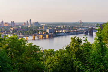 The tops of green leafy trees against the bridge across the river, connecting the two banks