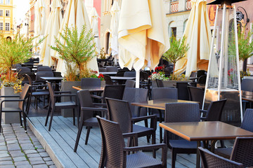 Outdoor cafe on sidewalk with empty tables and chairs with colorful plants and flowers in early summer morning in Poznan Poland.