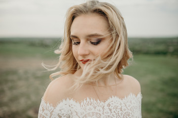 Fototapeta na wymiar Portrait of bride with hair flying in wind. Red lipstick. Face of beautiful woman. Closing her eyes with happy face expression, dreaming and enjoying warm summer wind while walking outdoors alone