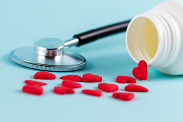 Pills in the form of heart on a blue background. Nearby is a stethoscope.