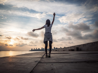 Fototapeta na wymiar Healthy lifestyle: A happy athlete walks after jogging and spread her arms in the sides against the backdrop of the city and sunset.