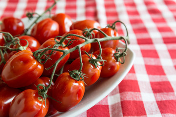 Pomodori freschi maturi su gambo dentro a piatto bianco su tovaglia a quadri