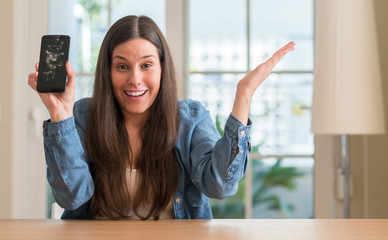 Brunette young woman holding broken smartphone very happy and excited, winner expression...