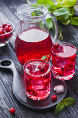 Red cherry cocktail with ice and fresh mint on a black wooden table