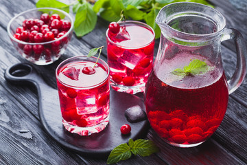 Red cherry cocktail with ice and fresh mint on a black wooden table