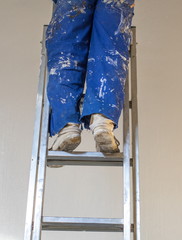 Legs of a person wearing a blue paint-stained overall standing on a ladder image with copy space in portrait format