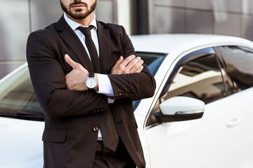 cropped image of businessman standing with crossed arms near car
